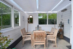 A covered patio with a table and chairs, large windows, and a lantern.