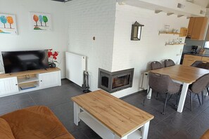 A modern living room with a fireplace, a dining area, and a kitchen with wooden cabinets.