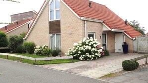 A two-story brick house with a red-tiled roof, a front door, and a small garden with white flowers. - Bungalow in Breskens near the Lighthouse (Breskens)