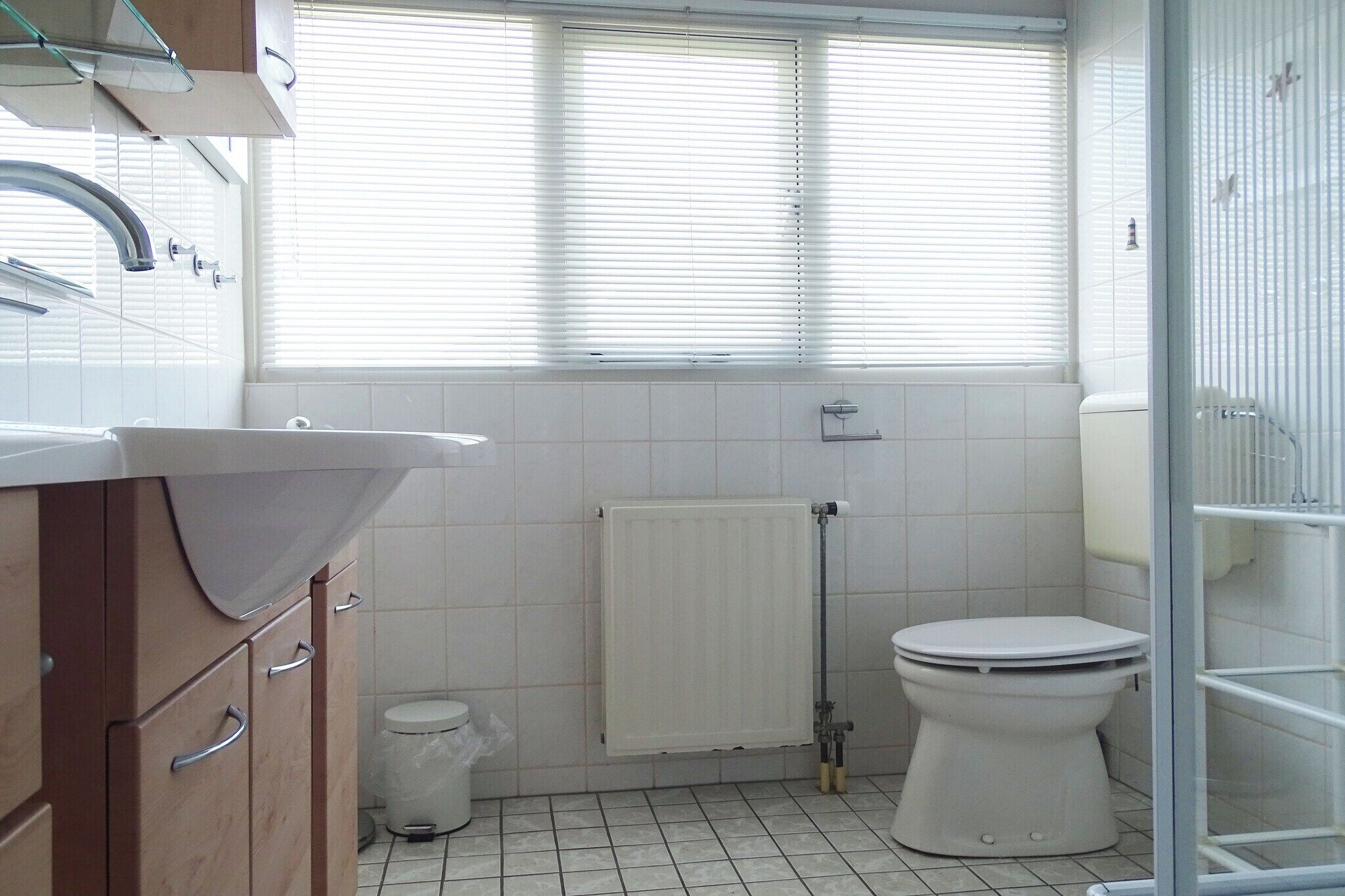 A bathroom with a toilet, a sink, a shower, and a window with blinds.