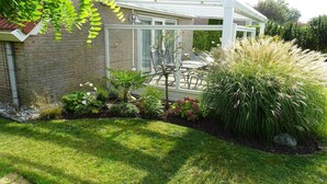 A conservatory with a glass roof, a brick house, and a garden with various plants and a lawn. - Bungalow in Breskens near the Lighthouse (Breskens)