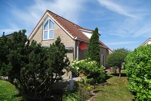 A house with a sloped roof, a chimney, and a garden with various plants and trees.
