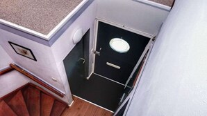 Une petite pièce fermée, dotée d’une porte, d’un luminaire et d’un escalier en bois.