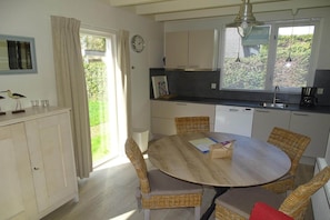 Una cocina con una mesa de comedor, sillas de mimbre, un reloj y una ventana con persianas.