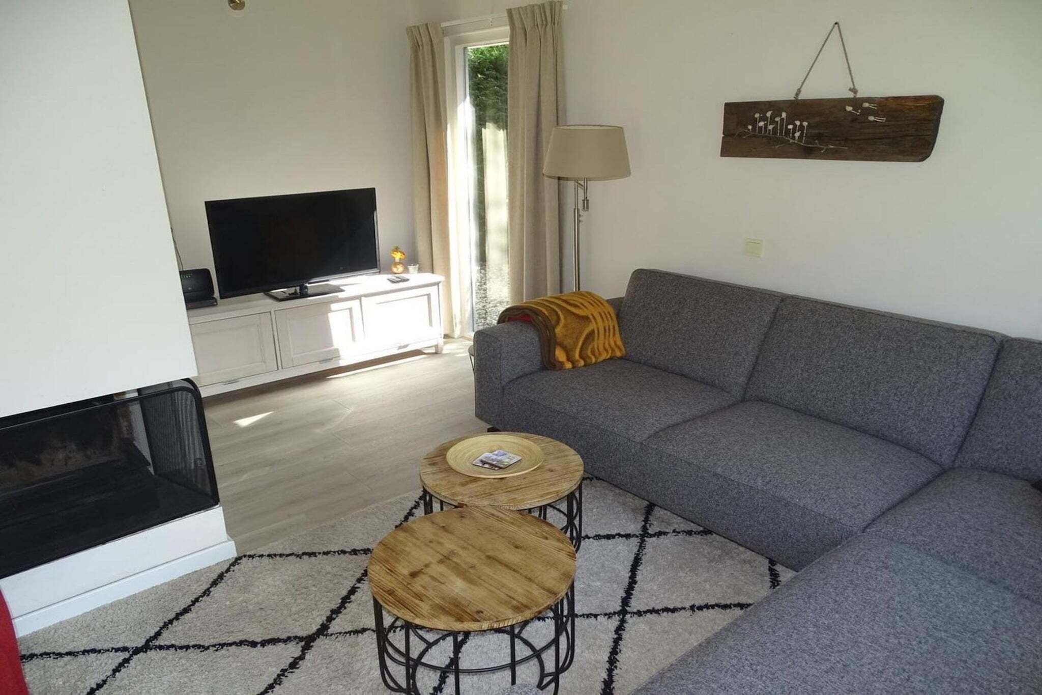 A living room with a sofa, two round wooden tables, a television, and a fireplace.