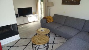 Un salon comprenant un canapé, deux petites tables rondes en bois, un téléviseur et une cheminée.