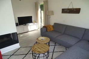 Una sala de estar con un sofá, dos mesas redondas de madera, un televisor y una chimenea.