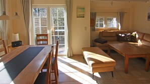 Un salón amplio con una mesa de comedor de madera, un sofá y una mesa de centro. Hay cortinas en las ventanas y un cuadro en la pared.