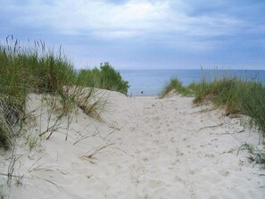 Ein Sandweg am Strand, umgeben von Gras, der zum Meer führt.
