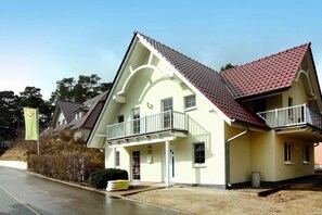 A two-story building with a balcony, a red-tiled roof, and a beige facade. - Doppelhaushalfte Strandhaus I in Trassenheide (Trassenheide)