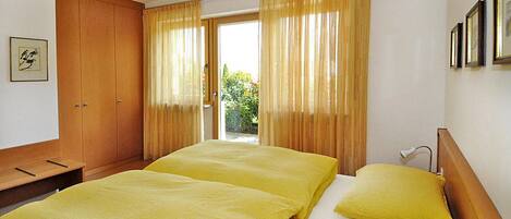 A hotel room with two beds, a wooden wardrobe, and a view of greenery outside.