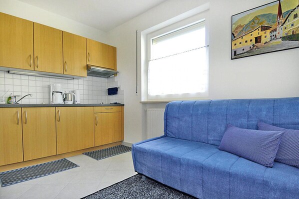 A compact kitchen with wooden cabinets, a blue sofa, and a window with a view of a building. - Apartment in Schlanders With Terrace (Silandro)