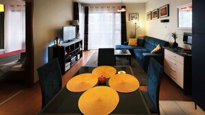 A modern living room with a sofa, a dining table with placemats, a television, and a kitchen area with a refrigerator. - Apartment in Swinoujscie Near the Beach (Swinoujscie)