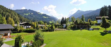 A residential area with a large green lawn, a swimming pool, and houses with a mountainous backdrop.