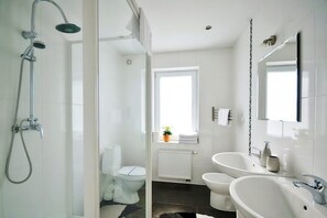 A modern bathroom with a shower, two sinks, a toilet, and a window with a plant. - Comfortable Holiday Apartment Close to the Beach (Ustronie Morskie)