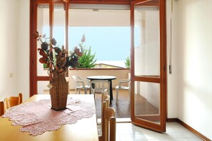 Ein Essbereich mit Tisch, Stühlen, einer Blumenvase und Blick durch eine Glastür in einen Außenbereich.