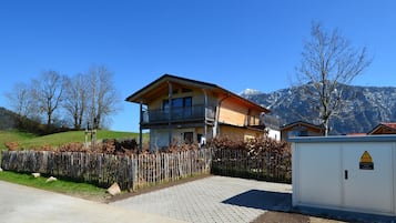 Situated in a mountainous region, this chalet-style building features a spacious balcony and a charming, vine-covered fence.