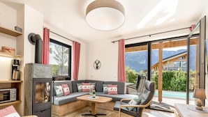 Una sala de estar moderna con sofá, sillón y mesa de centro, una chimenea y vistas a un paisaje montañoso.