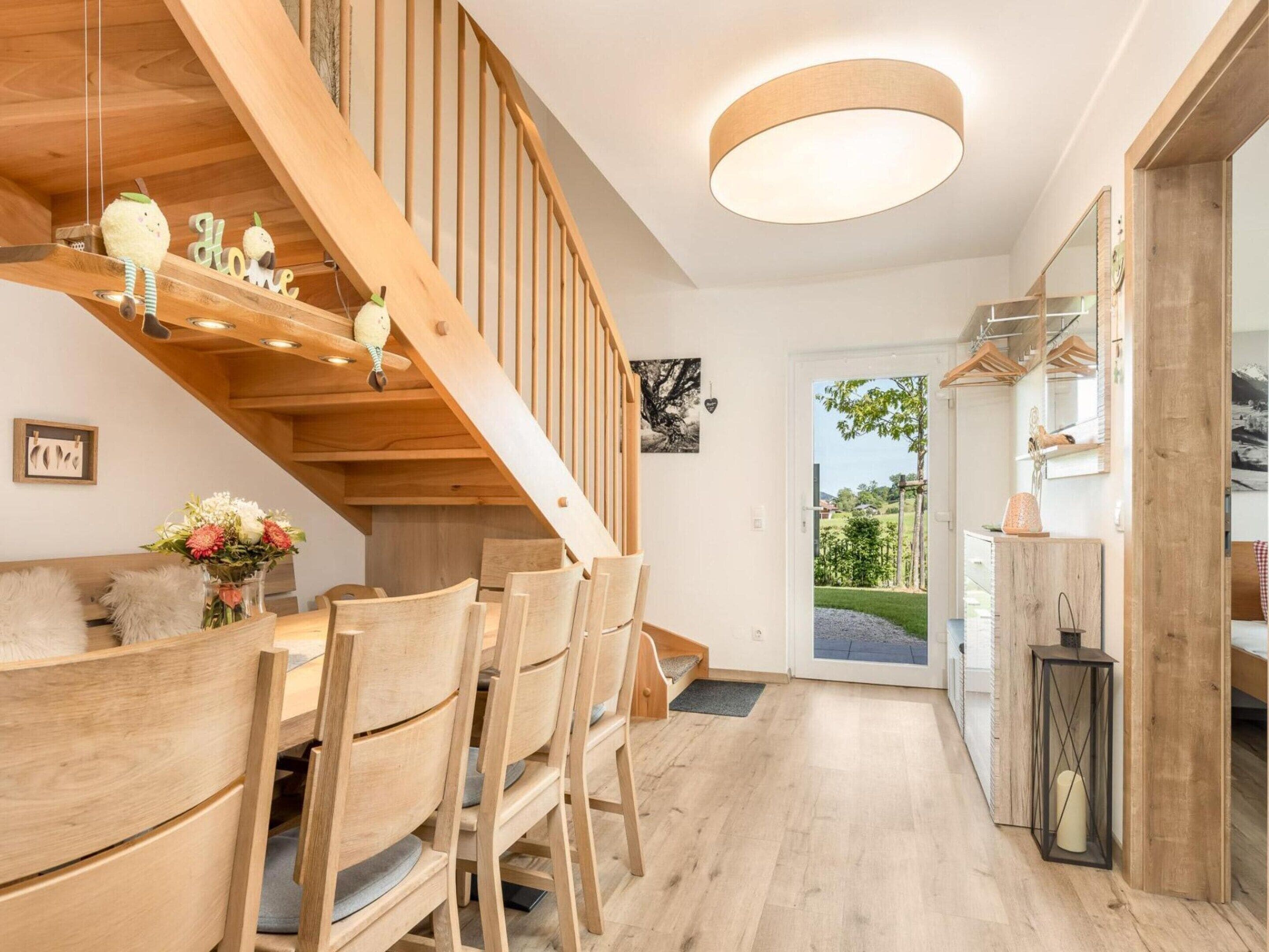 A wooden staircase leading to a dining area with chairs and a table, a hanging light fixture, and a view of the outdoors.