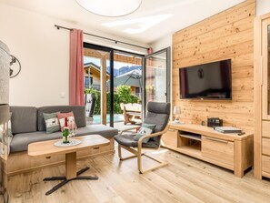 A modern living room with a sofa, a chair, a coffee table, a TV, and a wooden wall. - Chalet Alpenzauber mit Beheiztem Pool, Inzell (Inzell)