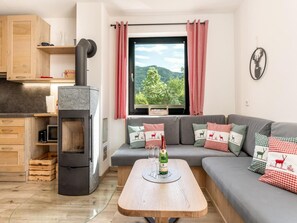 A cozy living room with a sofa, a table with a bottle, and a view of greenery outside. - Chalet Alpenzauber mit Beheiztem Pool, Inzell (Inzell)