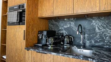 A compact kitchen with wooden cabinetry, a marble countertop, and modern appliances including a coffee maker and a kettle.