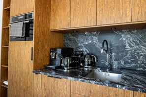 A compact kitchen with wooden cabinetry, a marble countertop, and modern appliances including a coffee maker and a kettle. - Holiday Home With Private Lake and Beach (Bytow)