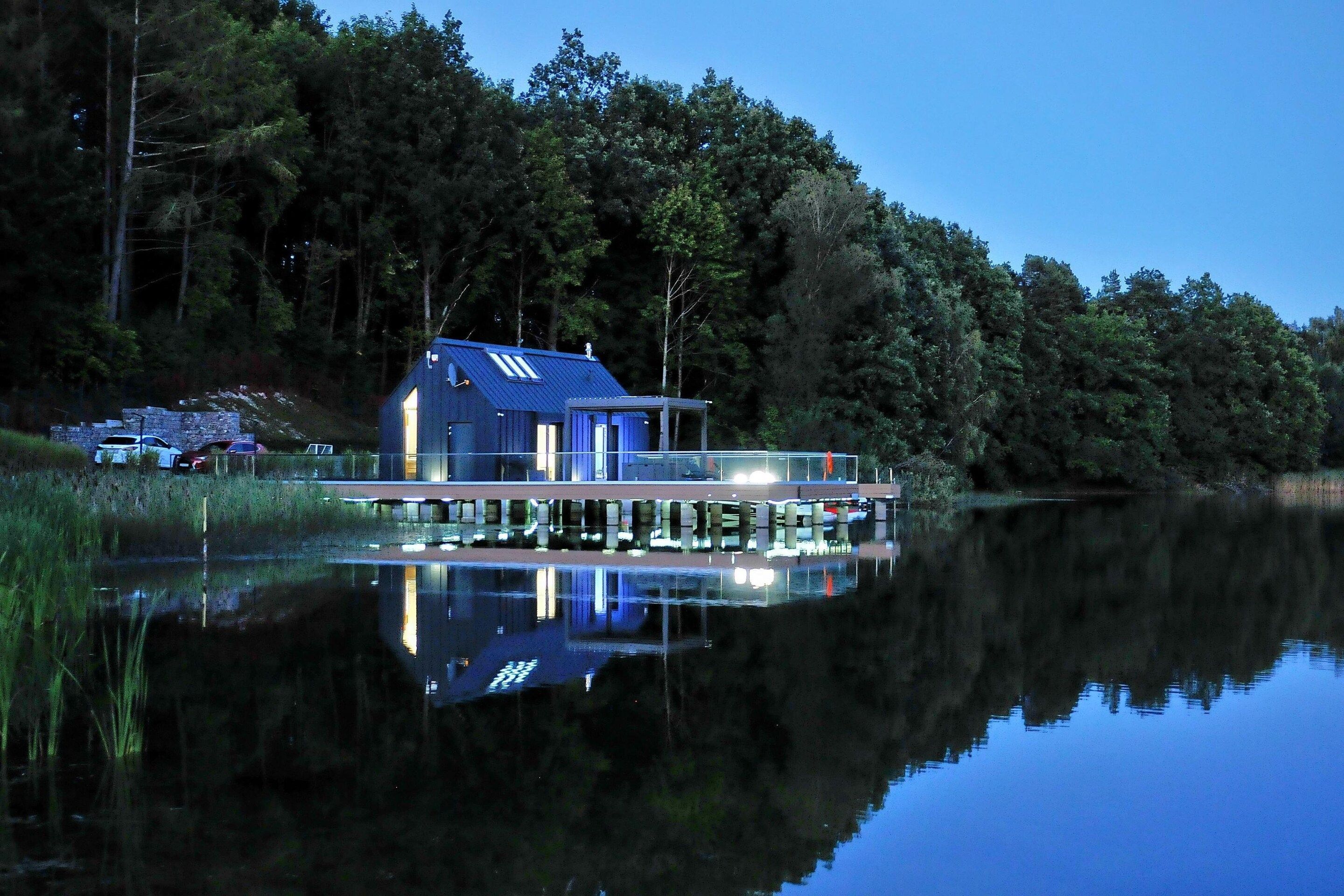 Ein Haus am Seeufer mit einem Steg, der ins Wasser ragt, umgeben von dichtem Wald.