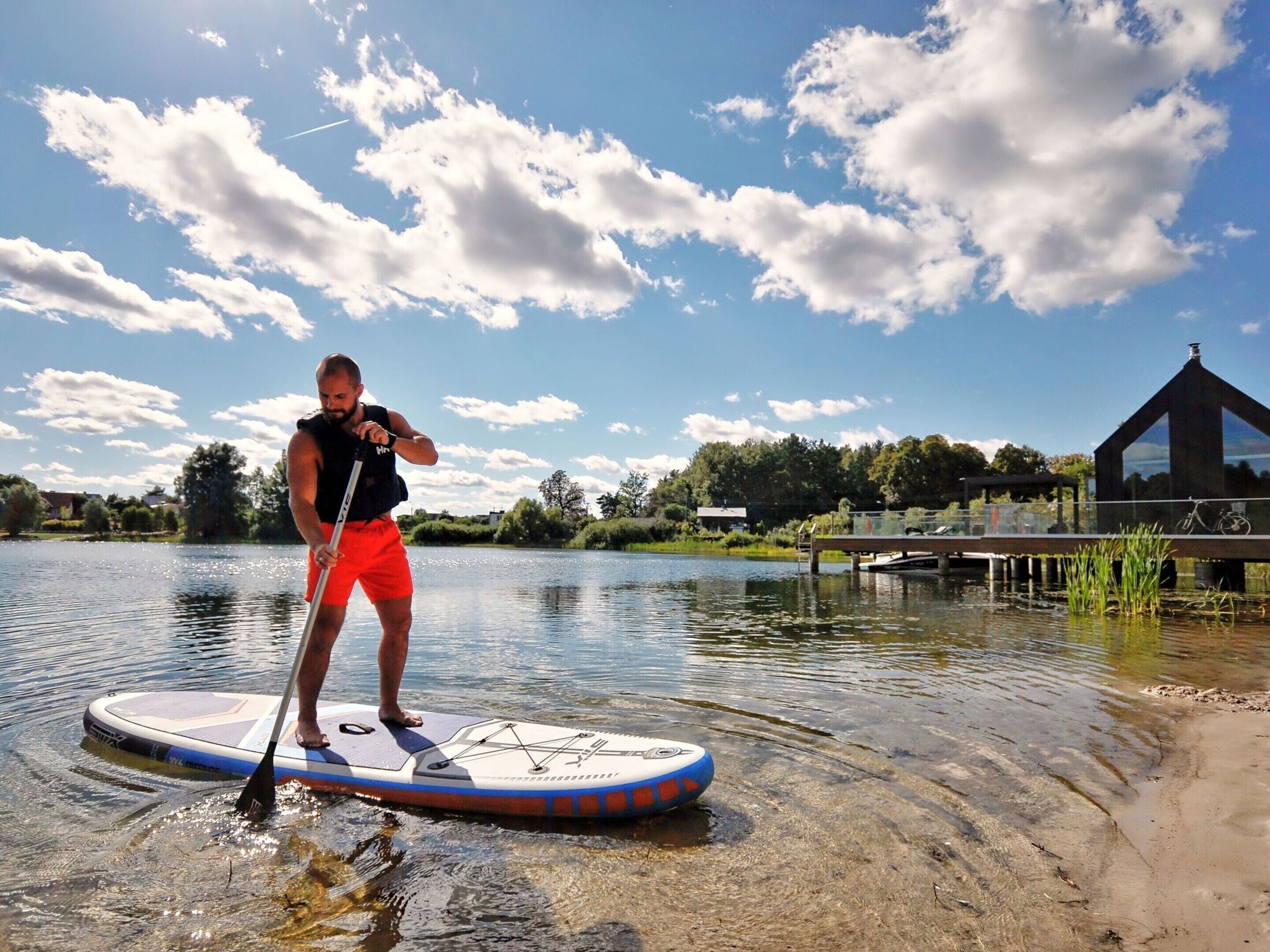 A person paddleboarding on a calm lake with a clear sky and a building in the background.