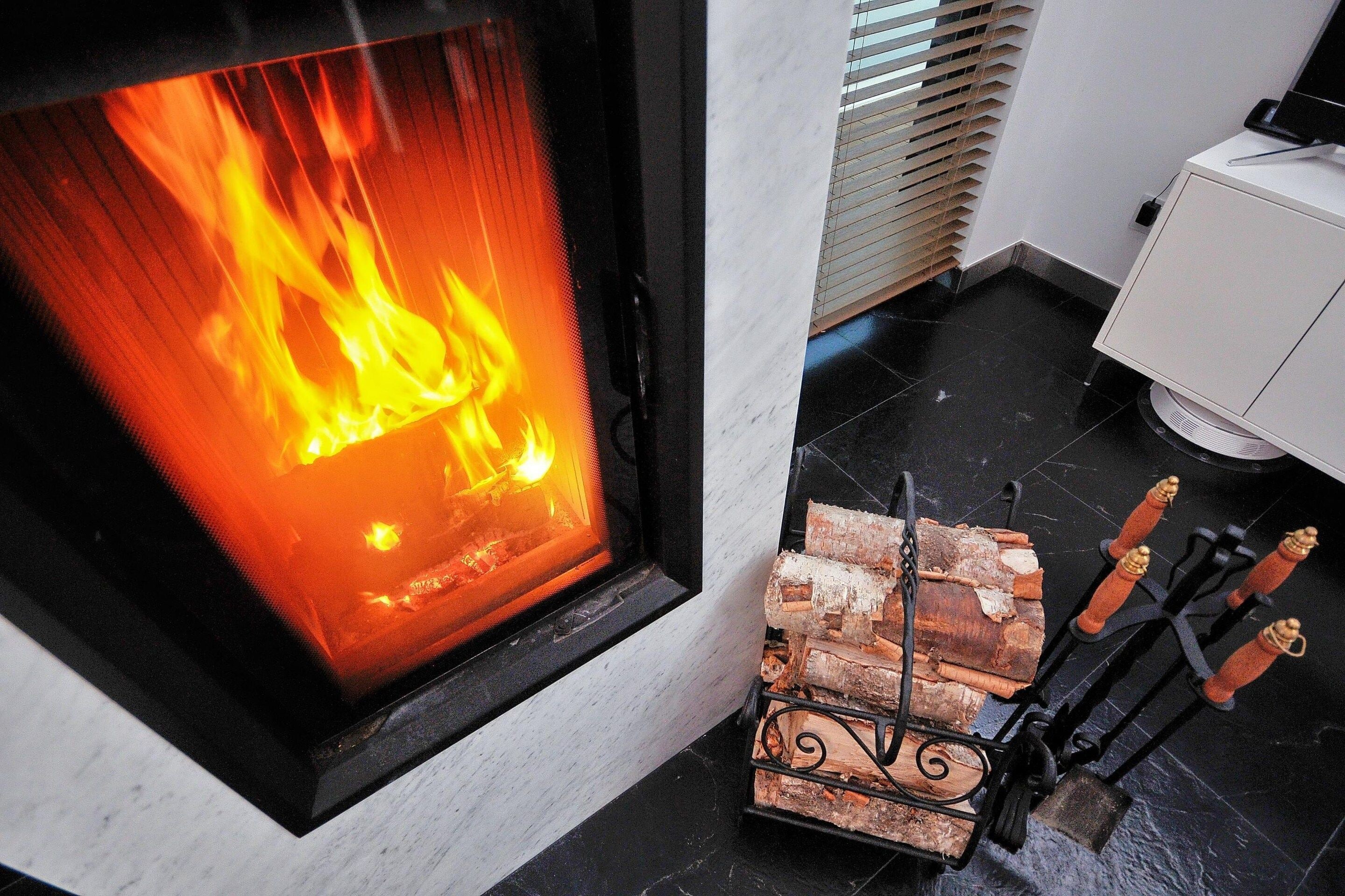 A fireplace with a visible fire, a log holder with logs, and a white cabinet.