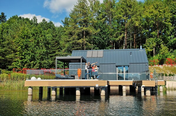 A modern houseboat with a deck, a covered area, and a glass railing. - Holiday Home With Private Lake and Beach (Bytow)