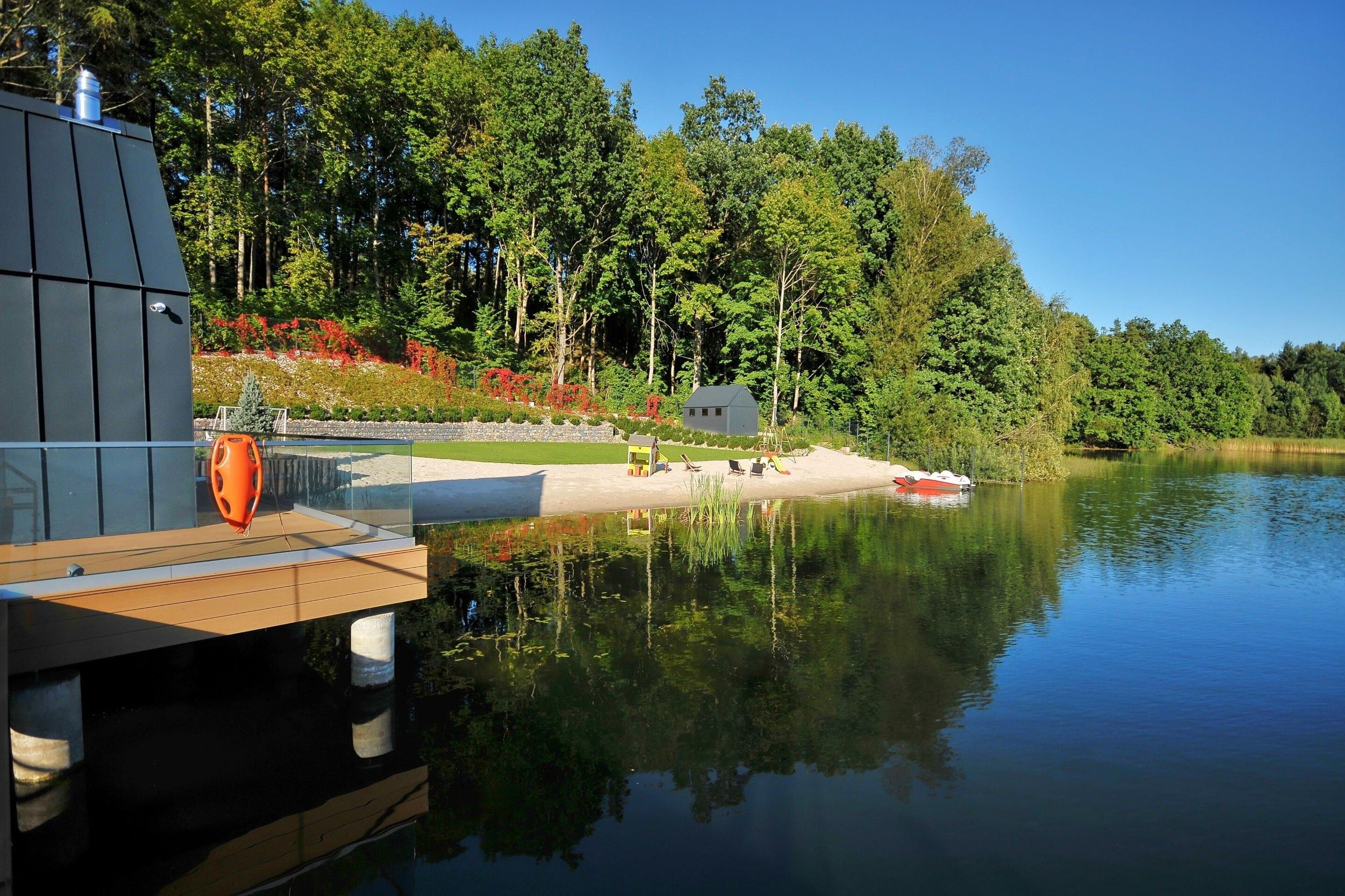 A lakeside cabin with a dock extending into the water, surrounded by dense forest and a clear sky.