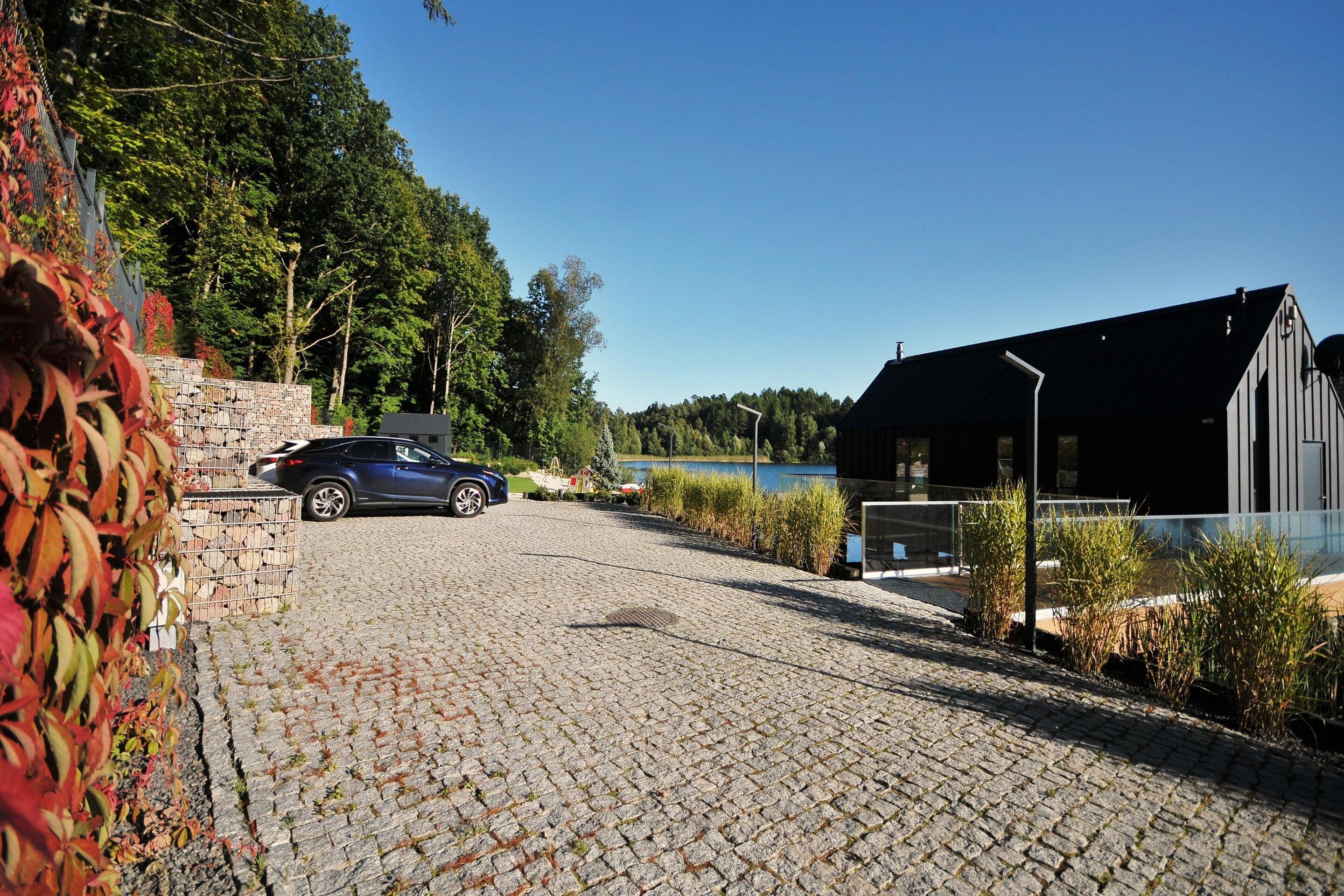 Asfaltoitu ajotie johtaa modernisti suunniteltuun rakennukseen. Edessä on pysäköity auto ja taustalla näkyy vesistö.