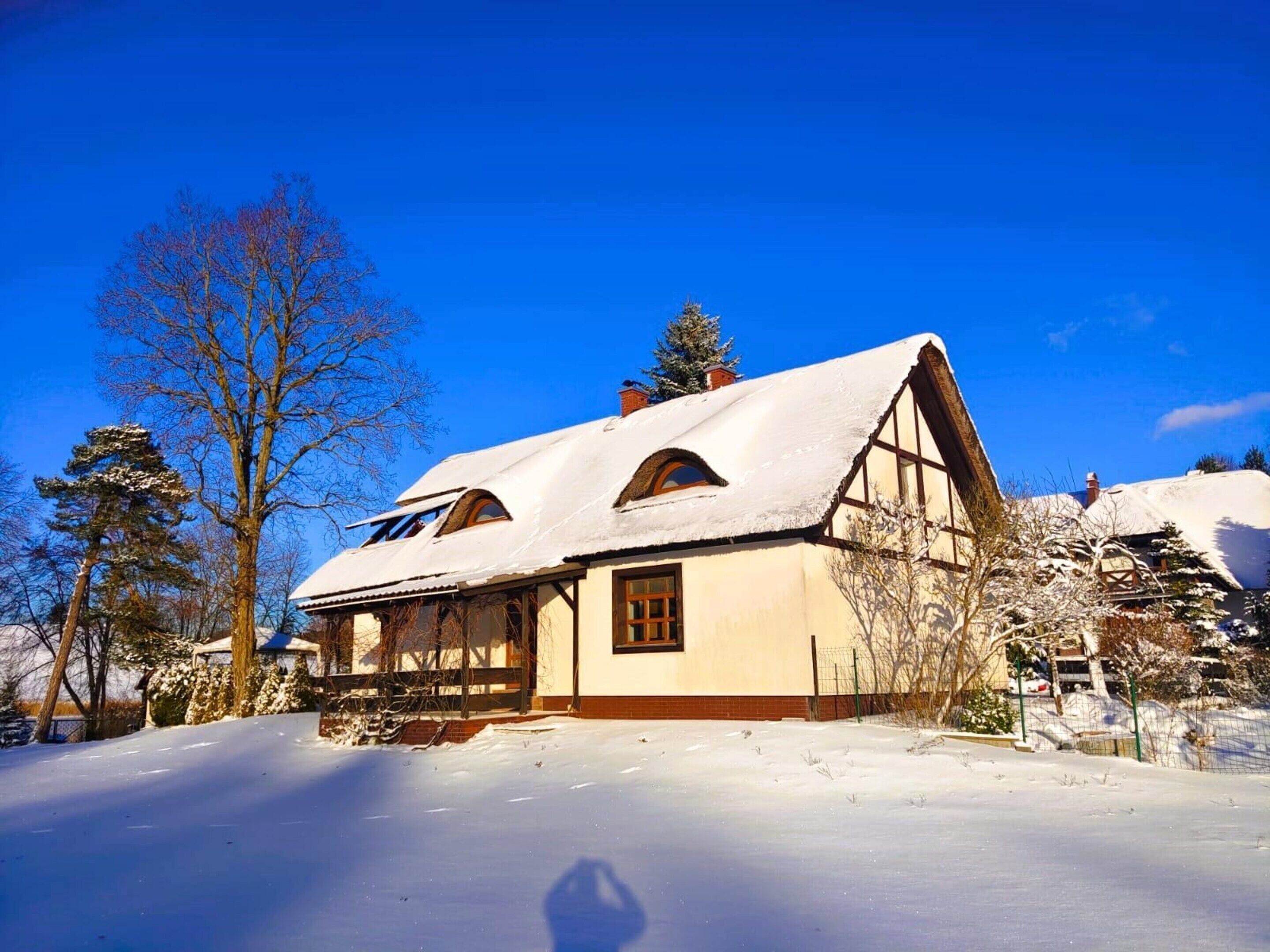 A traditional half-timbered house with a steeply pitched roof, surrounded by snow-covered ground and trees.