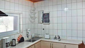 A kitchen with white tiles, wooden cabinets, a built-in oven, a coffee maker, and a window. - Holiday Home With Thatched Roof, Rekowo (Bytow)