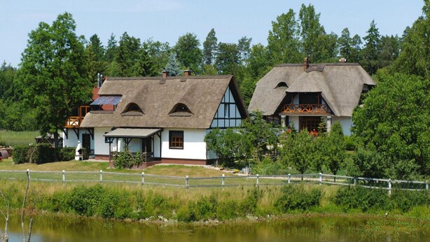 Two traditional houses with thatched roofs, surrounded by lush greenery and a pond. - Holiday Home With Thatched Roof, Rekowo (Bytow)