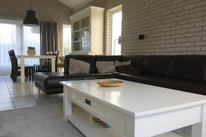 Een woonkamer met een zwarte leren bank, een witte salontafel en een bakstenen muur.