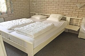 A white metal bed with two pillows and a blanket, a white nightstand, and a brick wall.