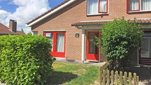 A two-story brick house with red doors and windows, a visible address sign, and a small garden area. - House in Breskens near the Beach (Breskens)