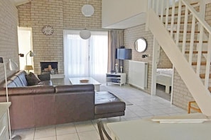 Een woonkamer met een bank, een salontafel, een open haard, een televisie en een trap.