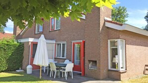 A two-story brick house with a patio area featuring a table and chairs, a white umbrella, and a red door. - House in Breskens near the Beach (Breskens)