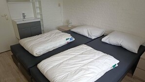 A room with two beds, a bedside table, a nightstand, a mirror, a sink, and a cabinet.