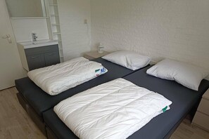 Ein Zimmer mit zwei Betten, einem Nachttisch, einem Spiegel, einem Waschbecken und einem Schrank.