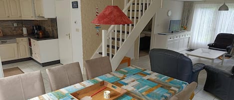 A dining area with a table set for four, a red hanging lamp, and a staircase leading to an upper level.