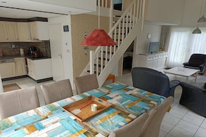 Un comedor con una mesa dispuesta para cuatro personas, una lámpara colgante roja y una escalera que lleva a un nivel superior.