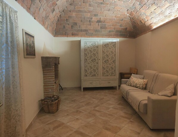 A cozy living room with a brick ceiling, a white floral cabinet, and a beige sofa. - Casa Daniela in Prata (Massa Marittima)