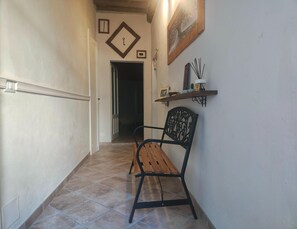 Un couloir avec un banc, une porte et une étagère ornée d’objets décoratifs.