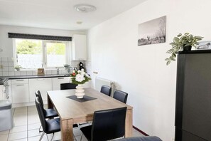 Une cuisine moderne avec des meubles blancs, une table à manger avec des chaises, une plante en pot et un radiateur.