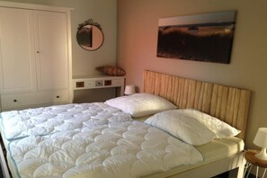 Ein Schlafzimmer mit Bett, Nachttisch, Lampe, Kleiderschrank, Spiegel und einem Bild an der Wand.