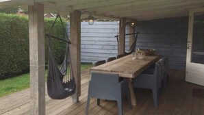 Une terrasse en bois avec une table et des chaises, un sac suspendu et un luminaire.